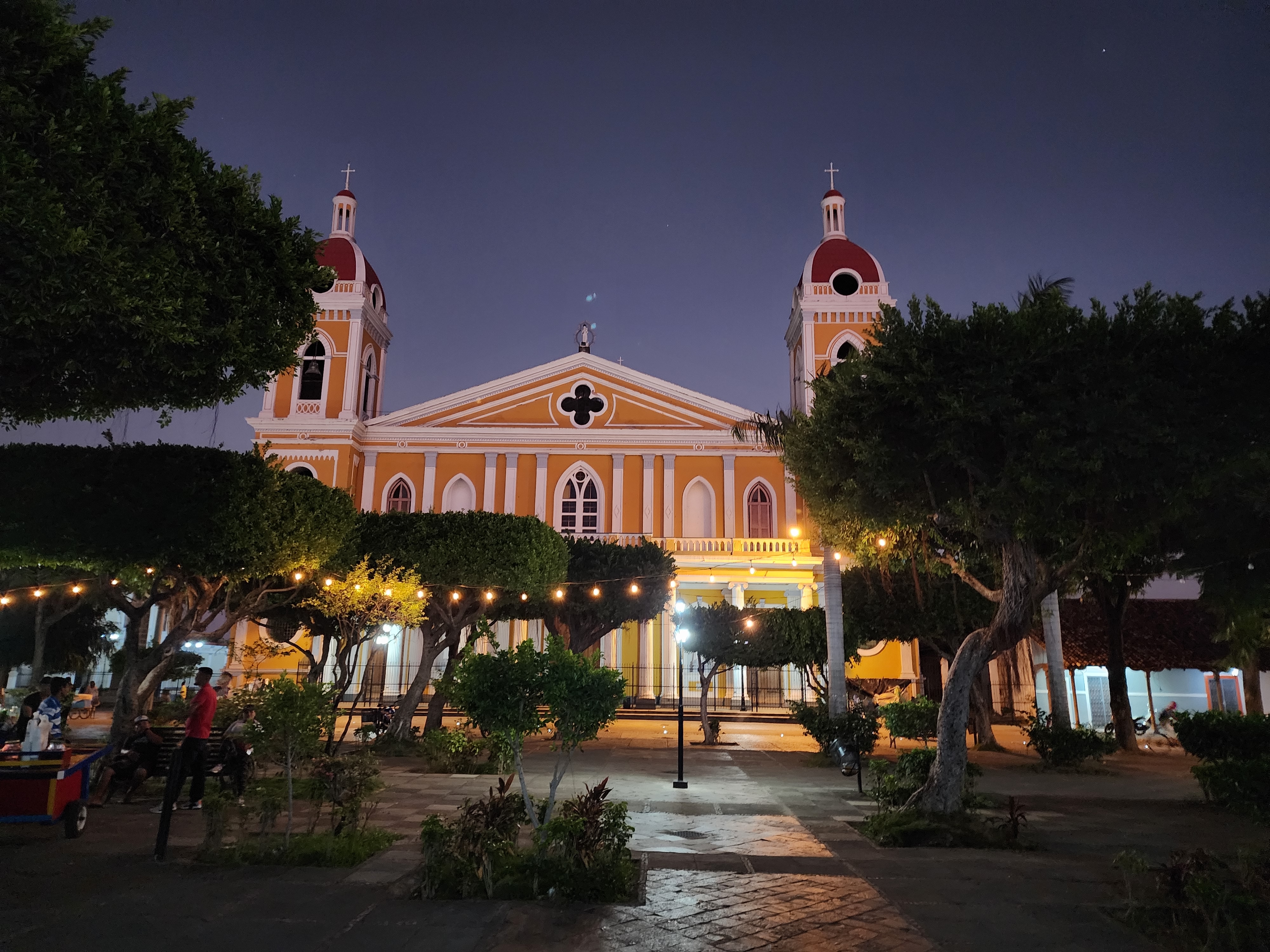 An orange and red church is lit up at night in the central square of Granada, Nicaragua