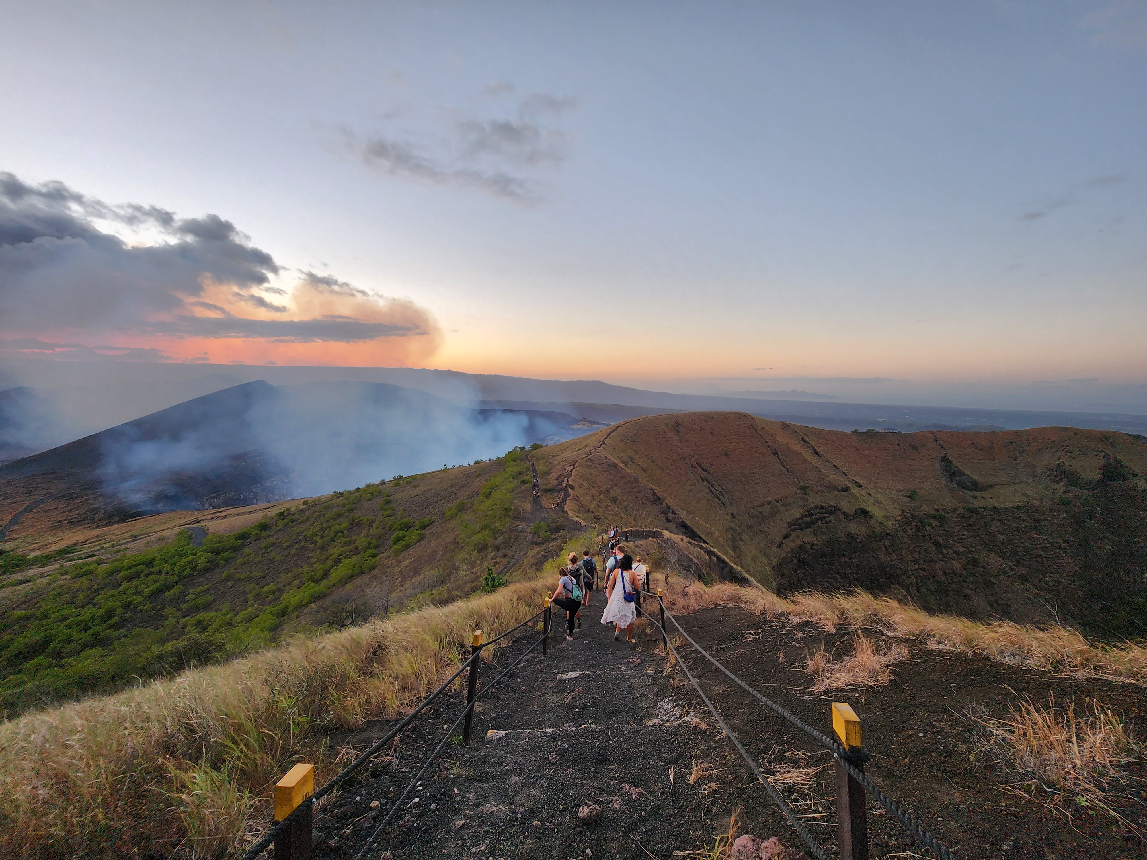 Hikers make their way down the ash covered path of a volcanic ridge at sunset