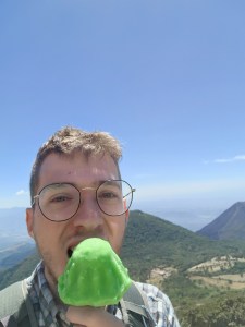 A man eats a green ice cream in front of a mountain view