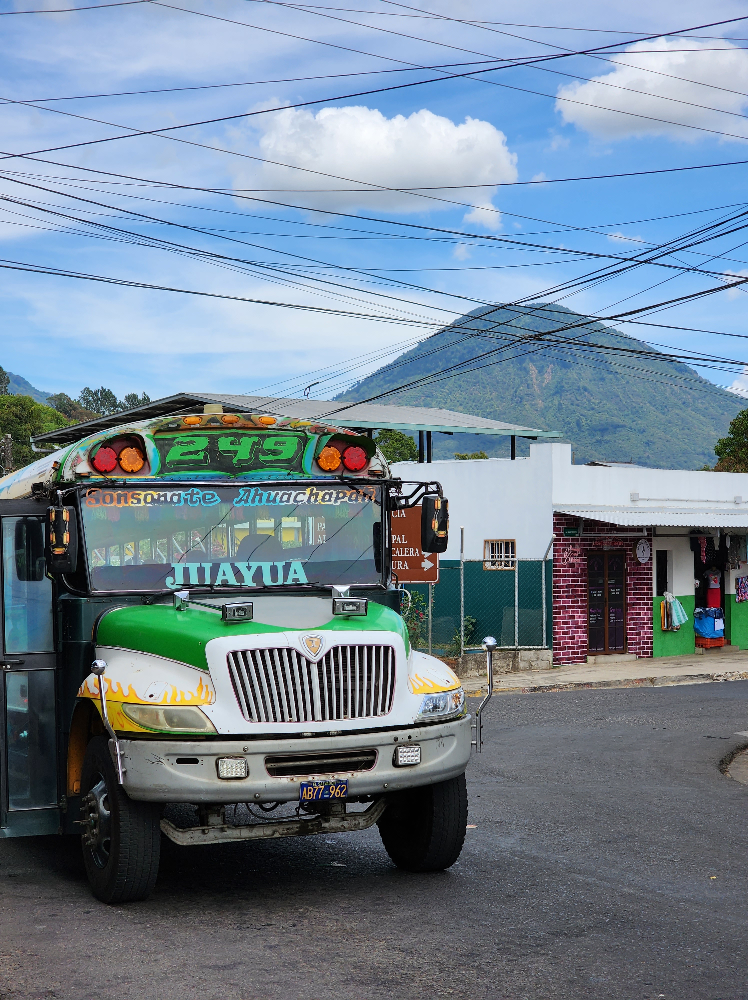 A colourful bus is parked on an El Salvadorian town with a large mountain in the background