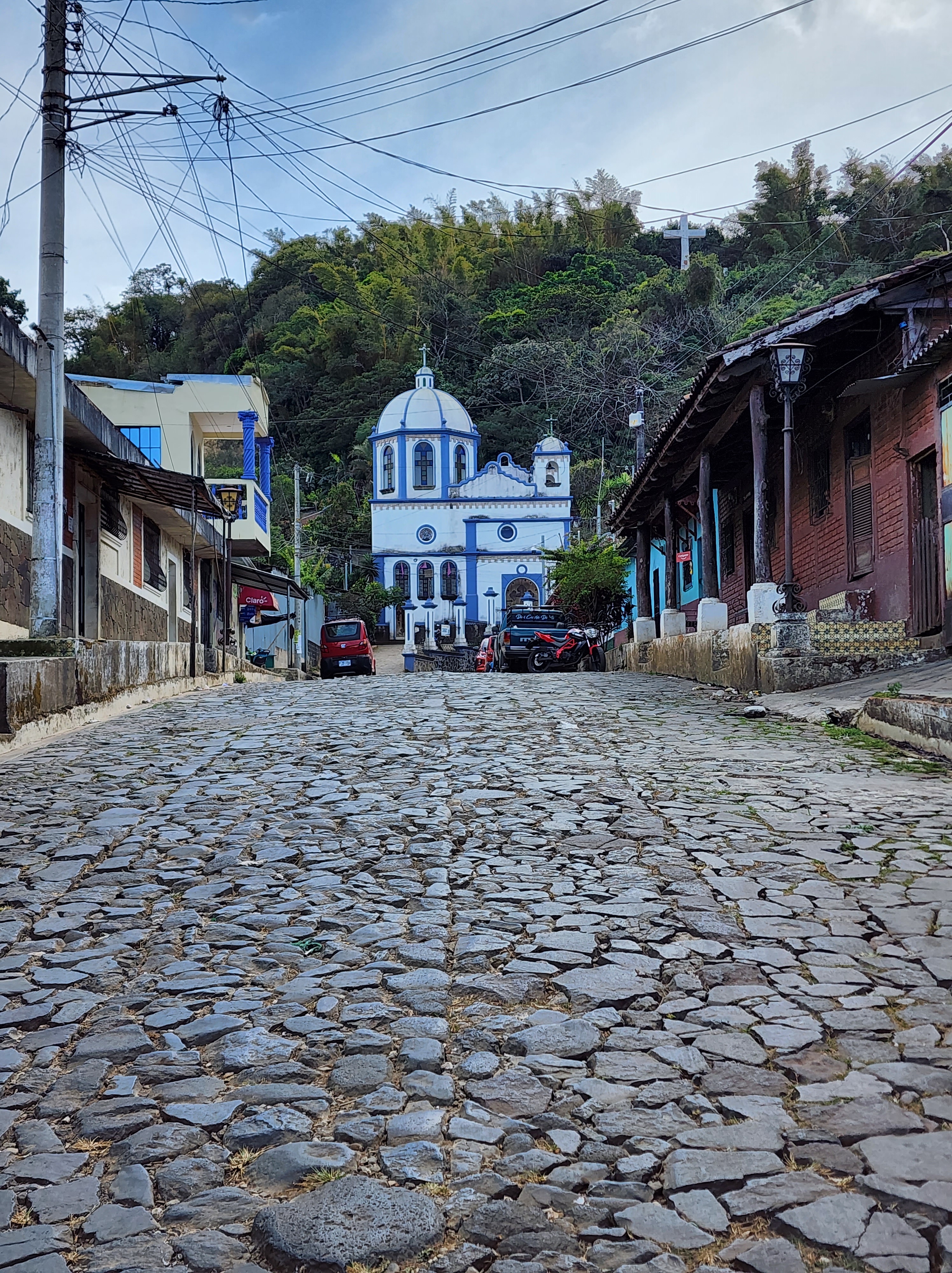 A cobblestone street leads to colourful blue and white church at the top of a hill in a town in El Salvador