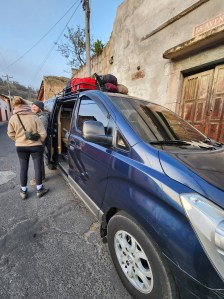 Two hikers lean on a blue van
