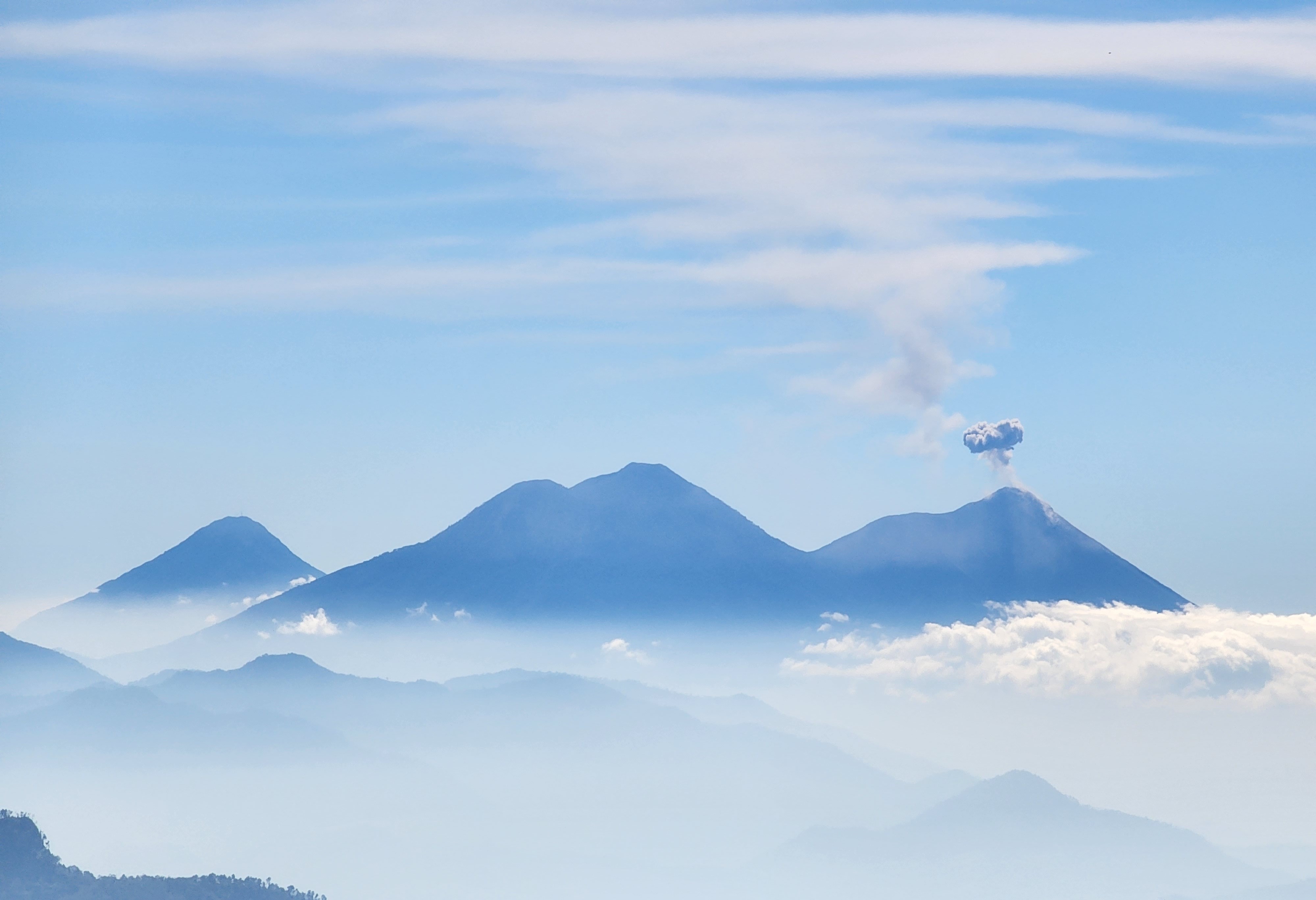 Three volcanoes are seen from a distance as one of them erupts and lets out a puff of smoke