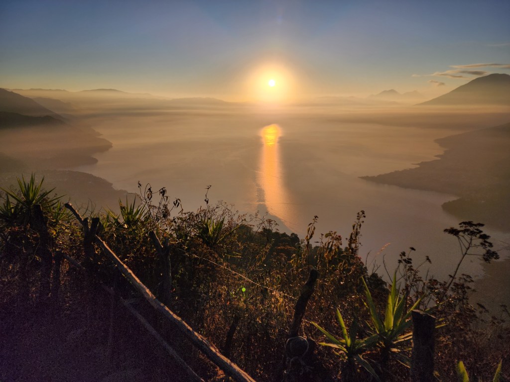 The sun rises up from behind Lake Atitlan, reflecting on the blue water and creating a beautiful shimmer over the lake and sorrounding hills and volcanos