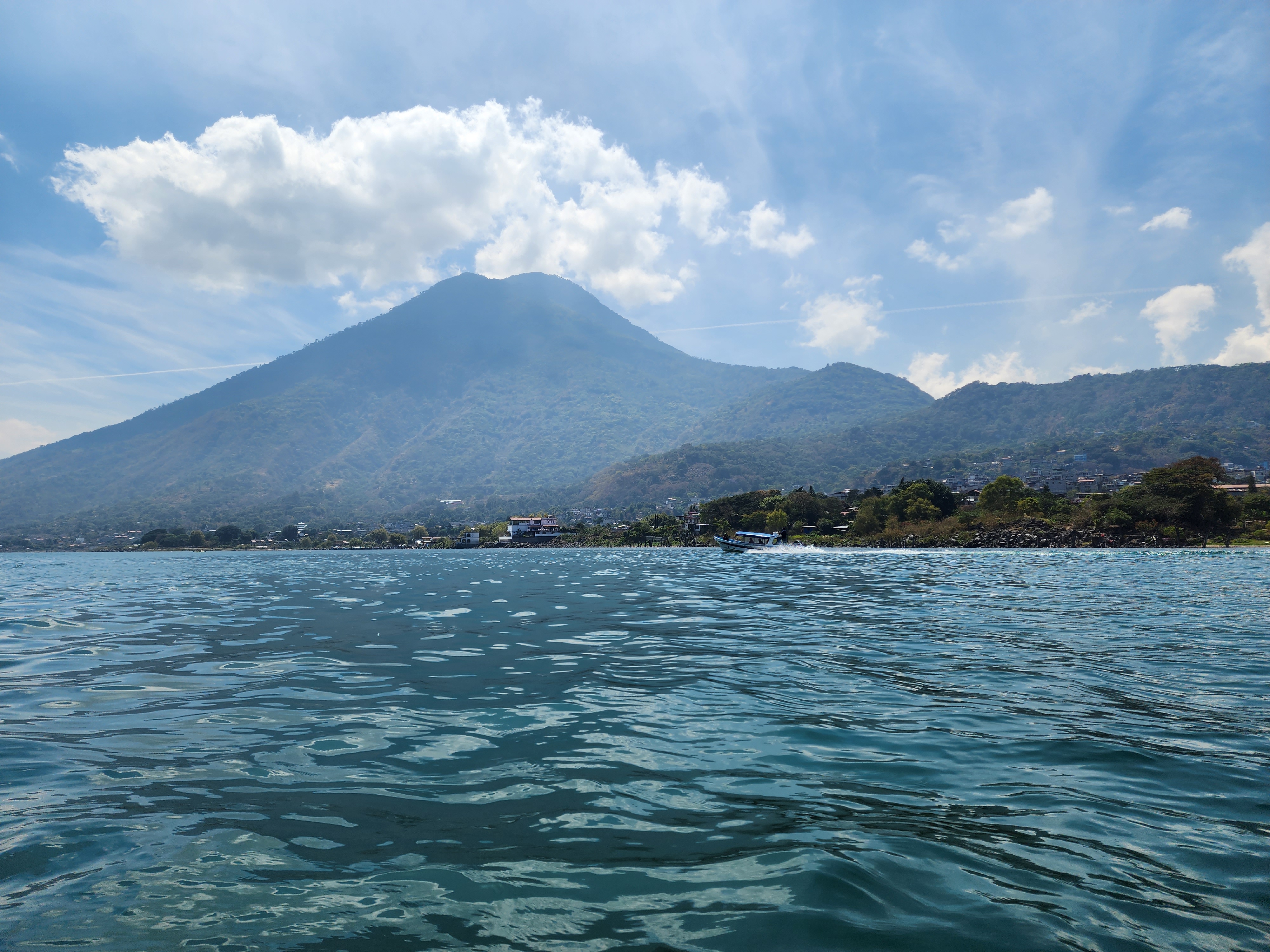 Volcan San Pedro standing tall over Lake Atitlan on a sunny day as a boat speeds by