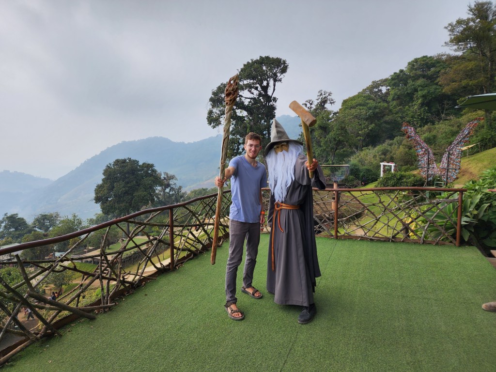 A man dressed up as Gandalf holds out his staff together with a young tourist on a viewpoint in Antigua
