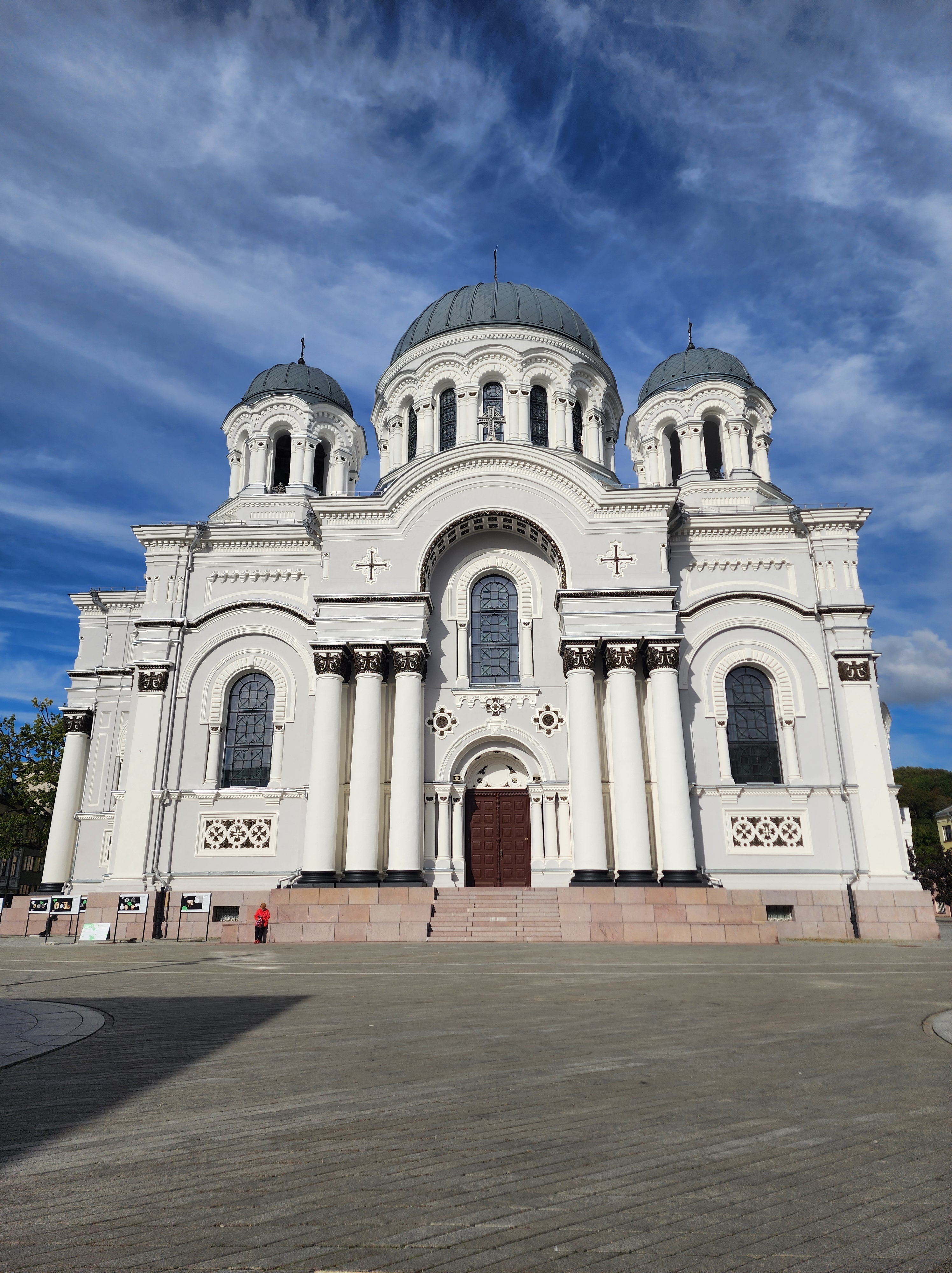 A large white basilica with three smaller towers stands in the clear blue sky of Lithuania