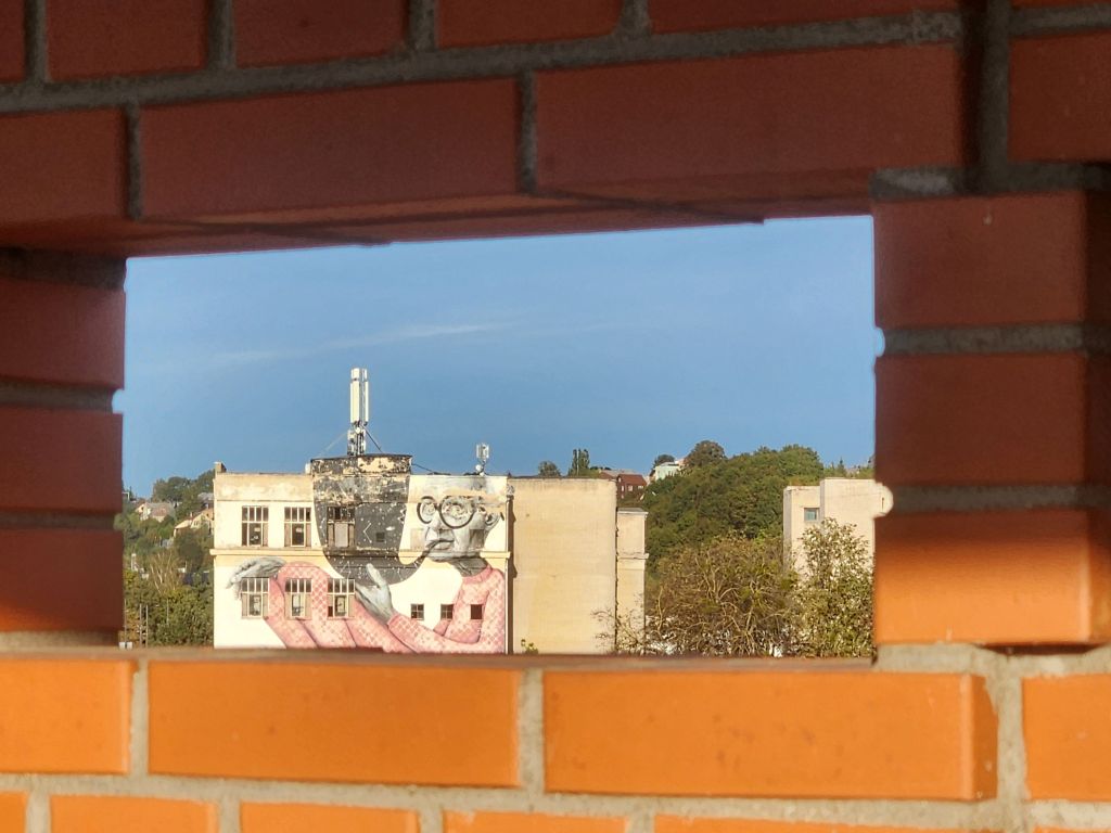A picture of a large mural of an old man smoking a massive pipe, taken through a small window in a brick wall