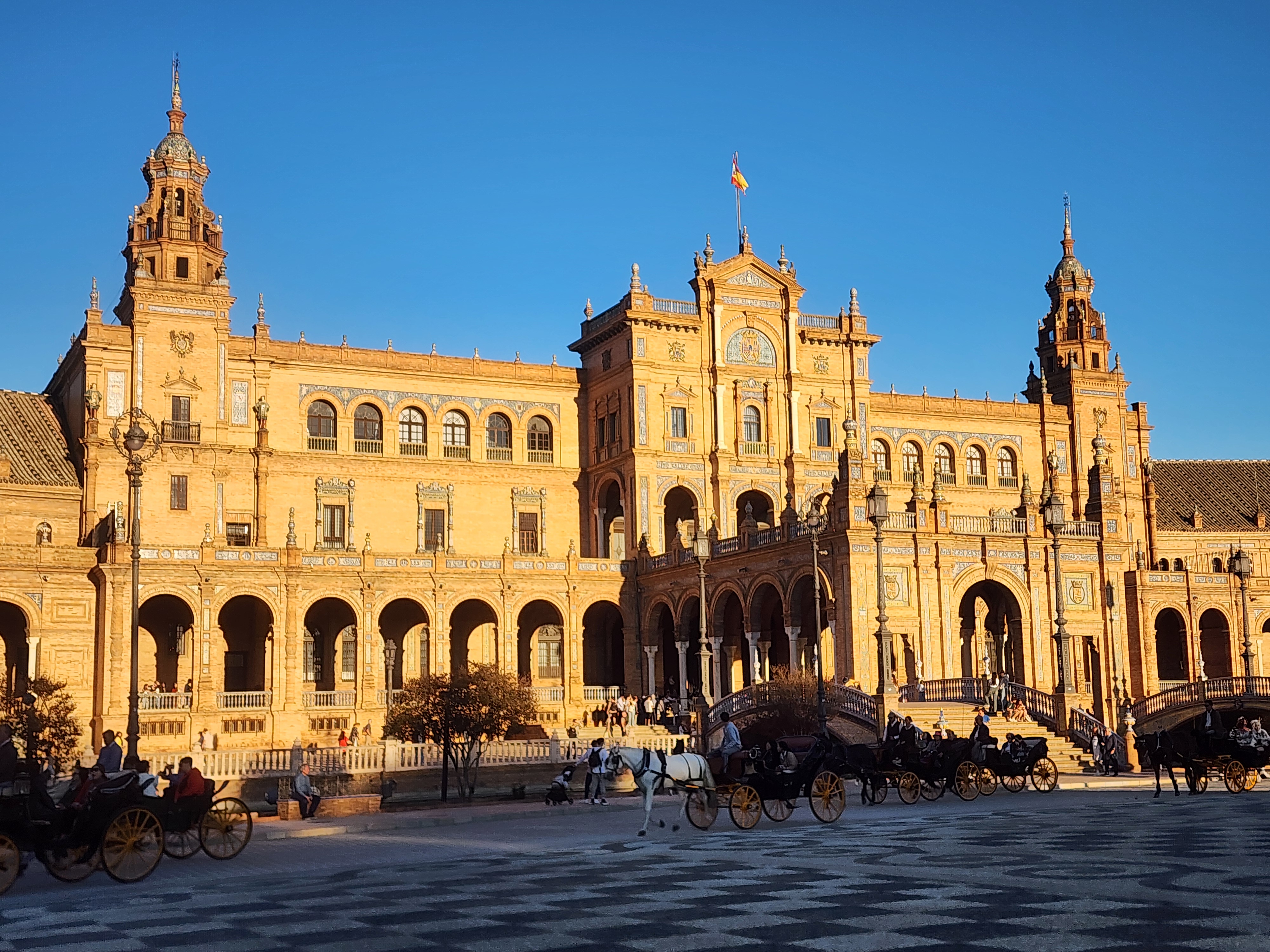 horses and carriages trot through Plaza de Espana in Seville on a sunny day.