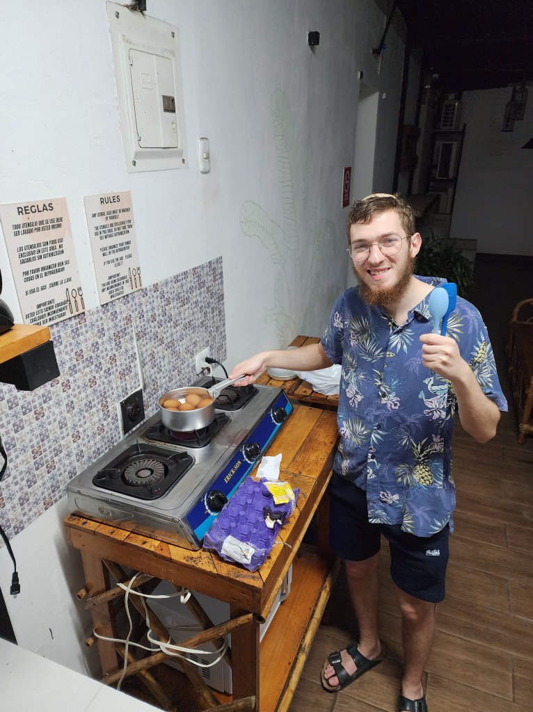 man in Hawaiian print shit boiling eggs in a hostel kitchen