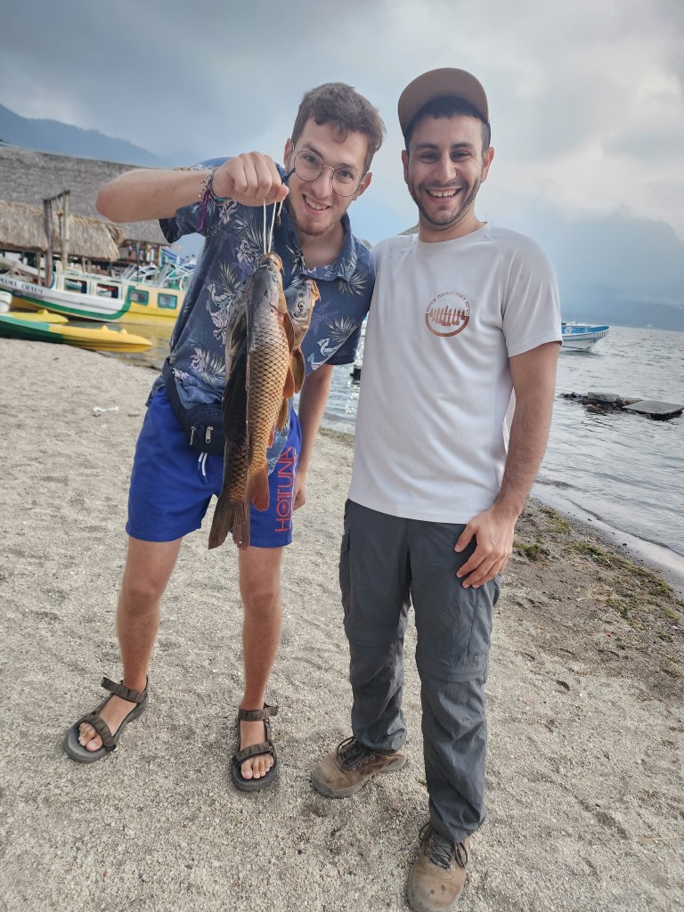 Two guys posing with fish they caught on a beach in Lake Atitlan