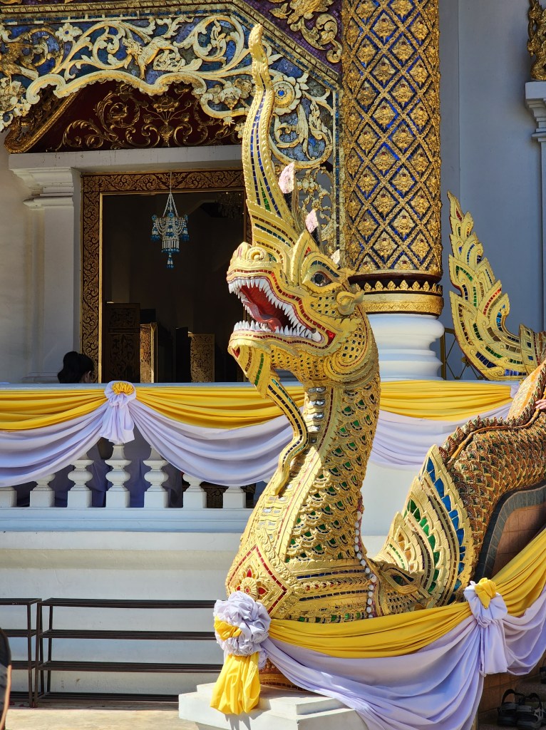 A gold and green sculpture of a serpent at a temple.