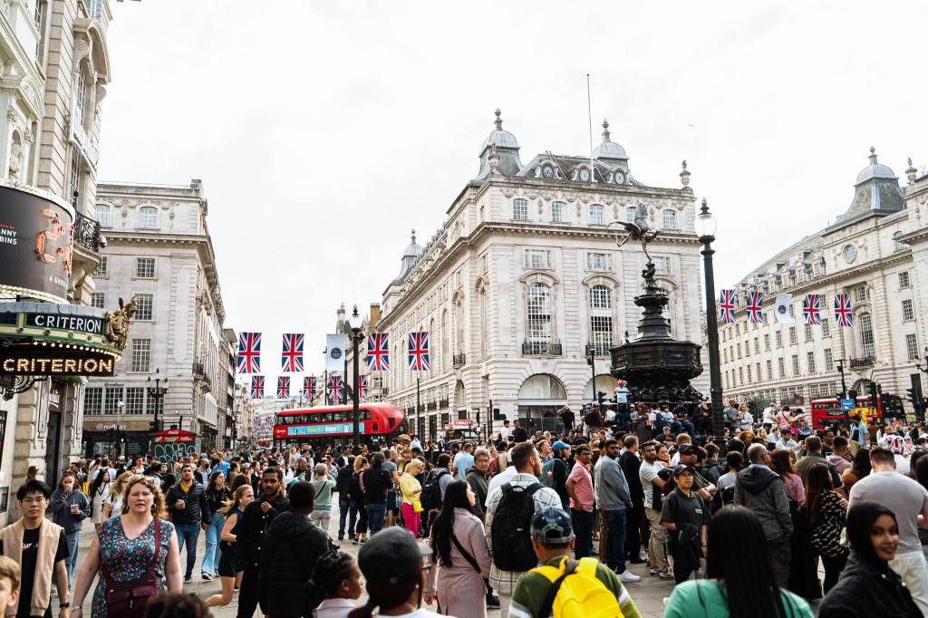 Piccadilly circus on a very busy day, with the Eros statue surrounded by tourists, and a bus going past in the background.