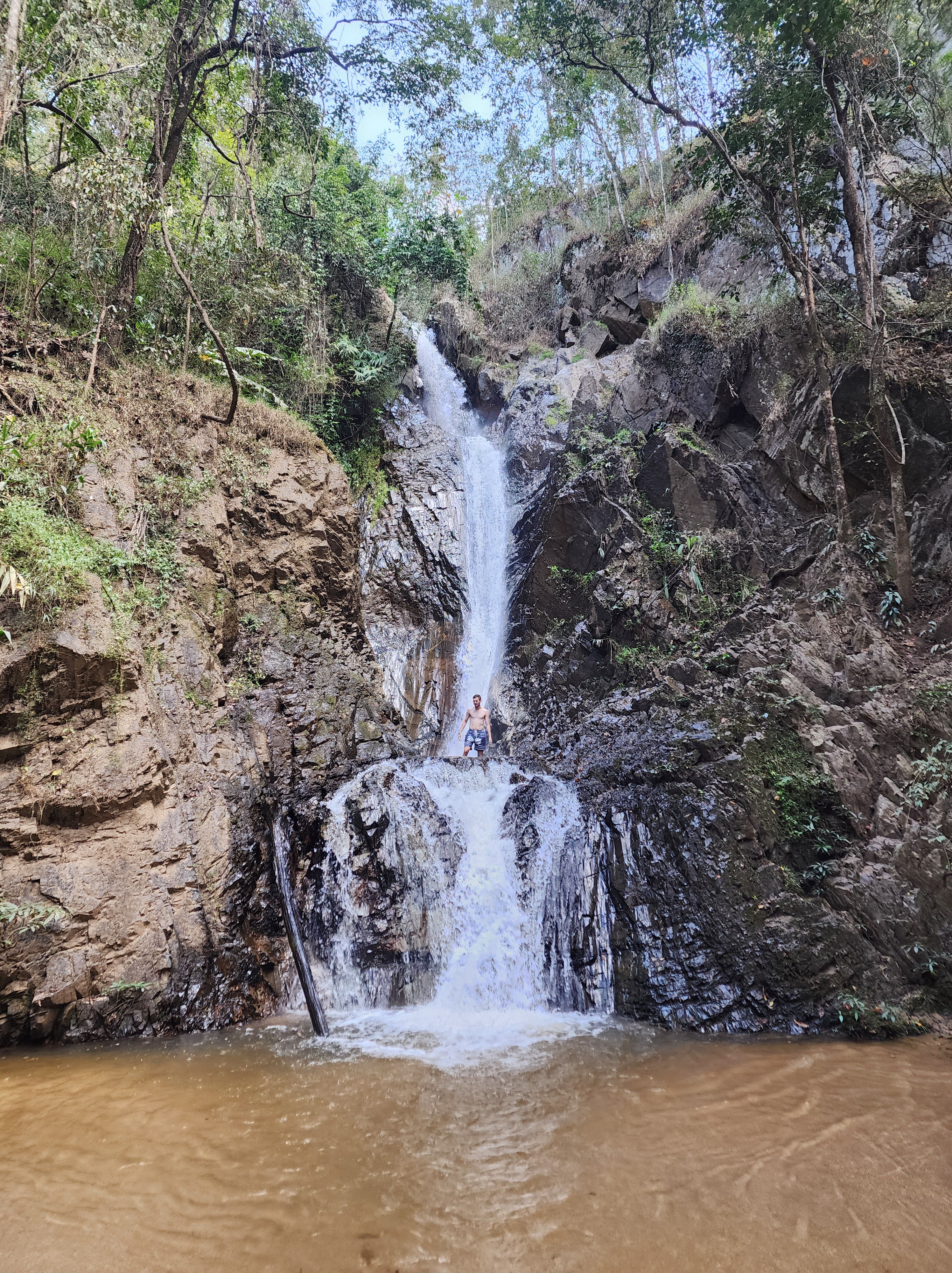 A man standing in the landing of a tall waterfalls middle tier.