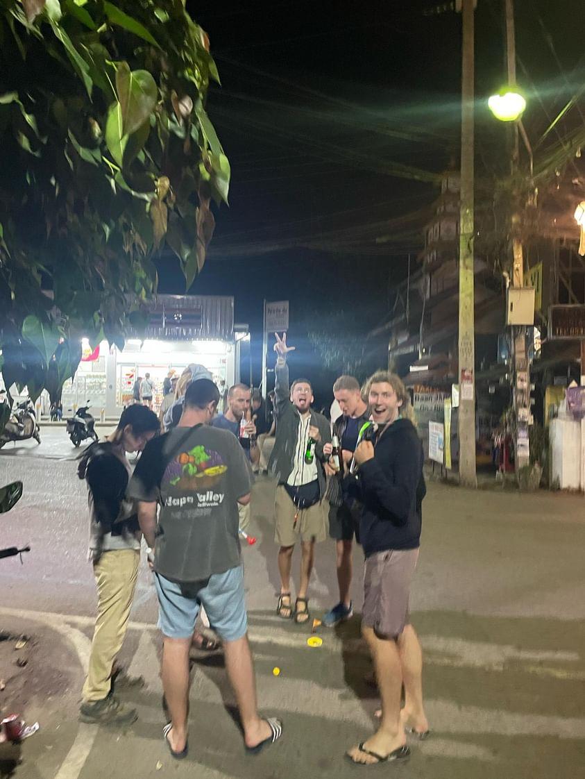 A group of young travellers playing mini golf on the side of the road with beers in their hands.