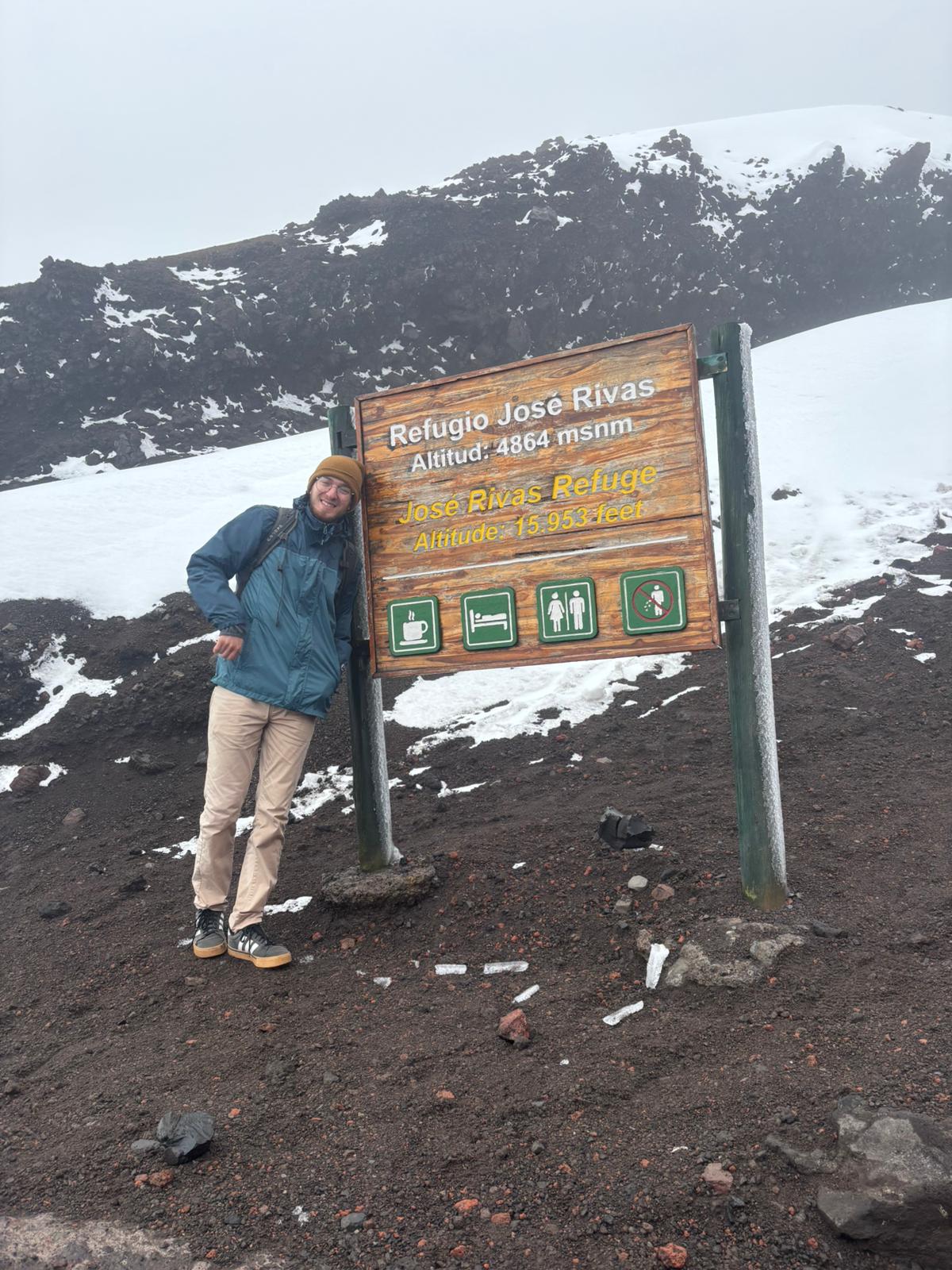 A hiker posing by a sign showing that he's reached Jose Rivas Refuge on Cotopaxi